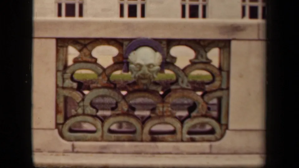 1940s 8mm closeup of decorative balcony artwork in Washington DC, showing a sculpted face within patterned metalwork.