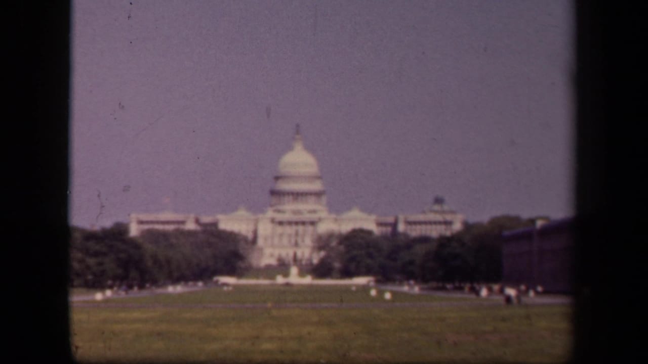 1943 8mm view of the U.S. Capitol in Washington, DC, seen across a broad lawn with trees and a pale sky.