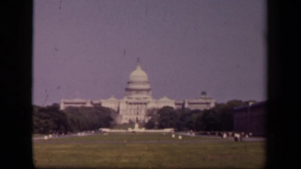 1943 8mm view of the U.S. Capitol in Washington, DC, seen across a broad lawn with trees and a pale sky.