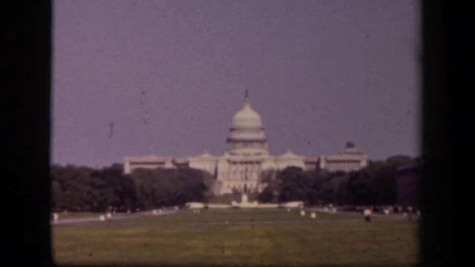 1940s home-movie frame of the U.S. Capitol from the lawn, with soft focus, trees, and dark scan edges.