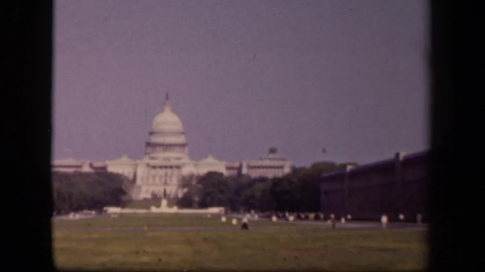 Soft 8mm view of the U.S. Capitol in Washington, DC, with open grass, trees, distant visitors, and dark gate borders at the sides.