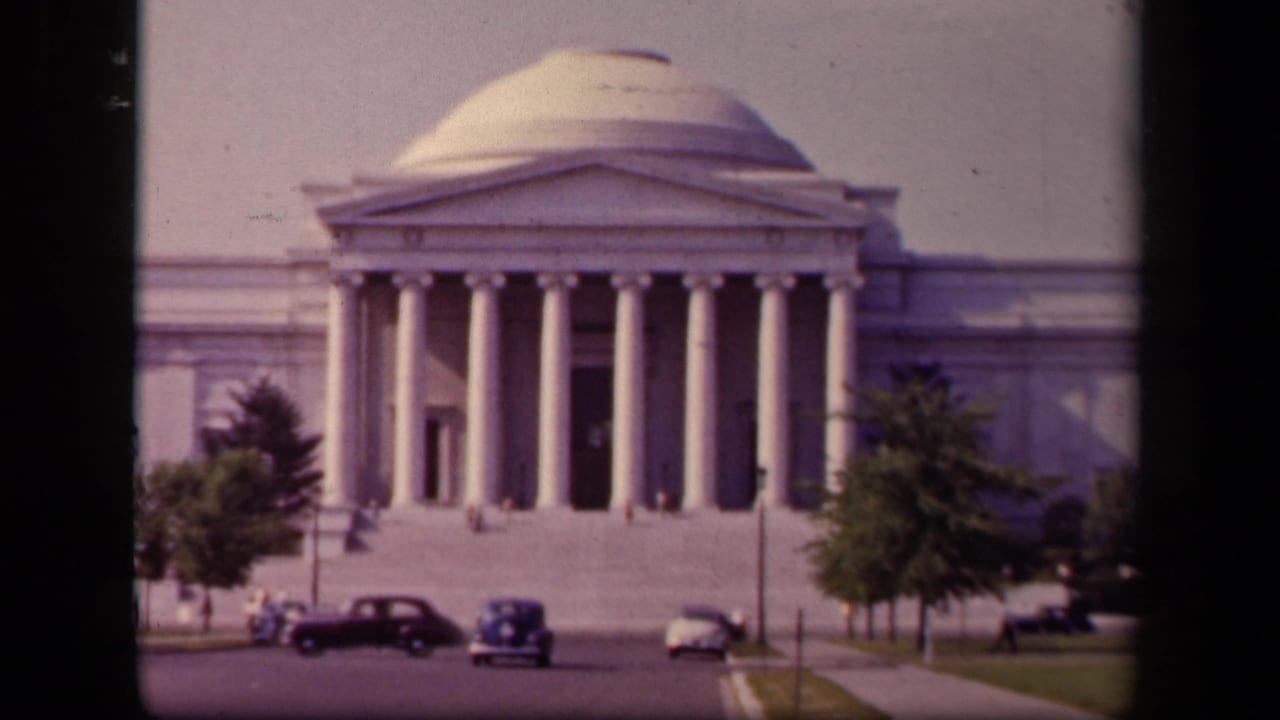 1943 Washington, DC home-movie frame showing the Jefferson Memorial facade, roadside traffic, trees, and small visitor figures.
