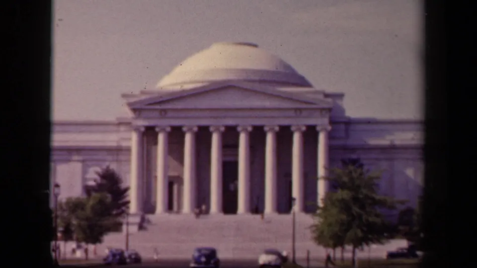 Soft 8mm frame of the Jefferson Memorial's columned front, with trees partly framing the steps and mid-century cars below.