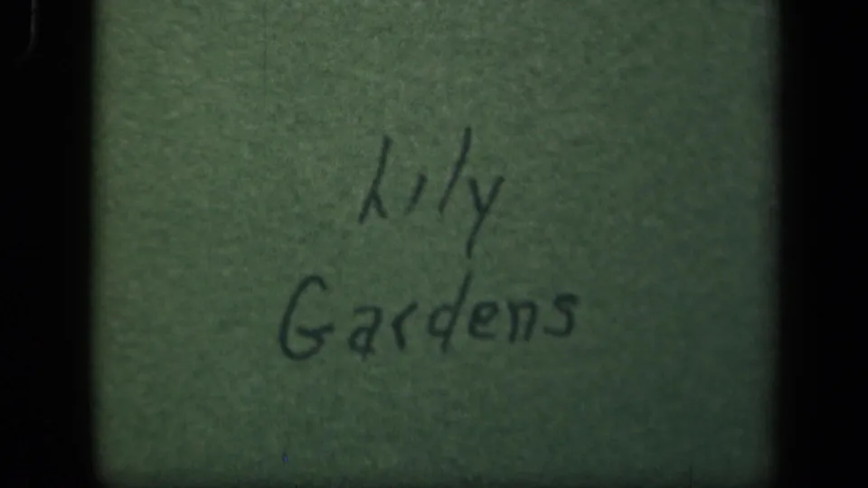 Green paper title card from the 1943 home movie, handwritten with the words Lily Gardens in dark ink.