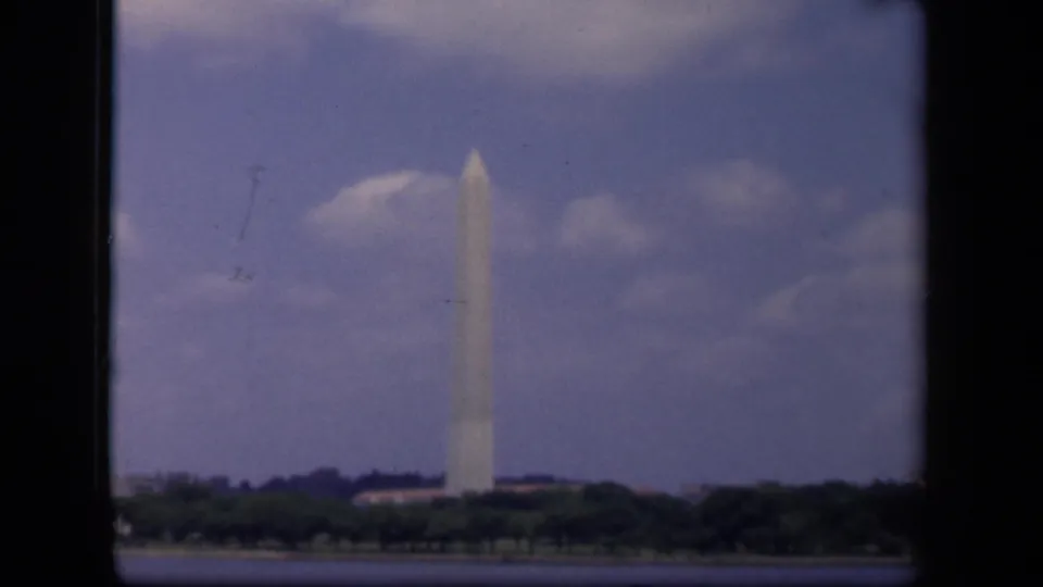 1943 8mm view of the Washington Monument across water, with a treeline and cloudy sky in Washington, DC.