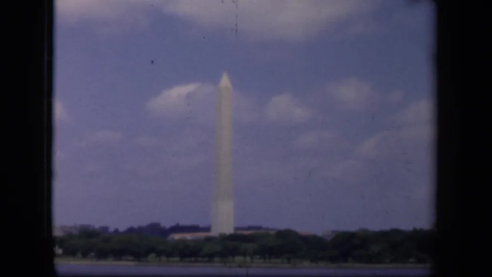 Washington, DC landmark view on 8mm film, showing the Washington Monument past a treeline and water.