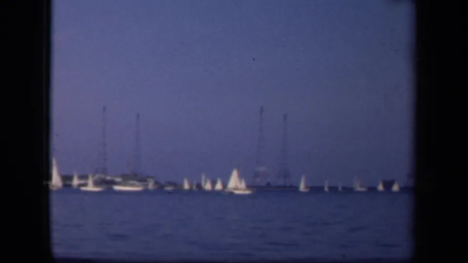 1943 Washington, DC home-movie frame showing small sailboats on blue water with distant utility towers along the horizon.