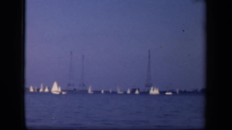 A wide 1943 home-movie view of sailboats on blue water in Washington, DC, with distant utility towers and a low shoreline.