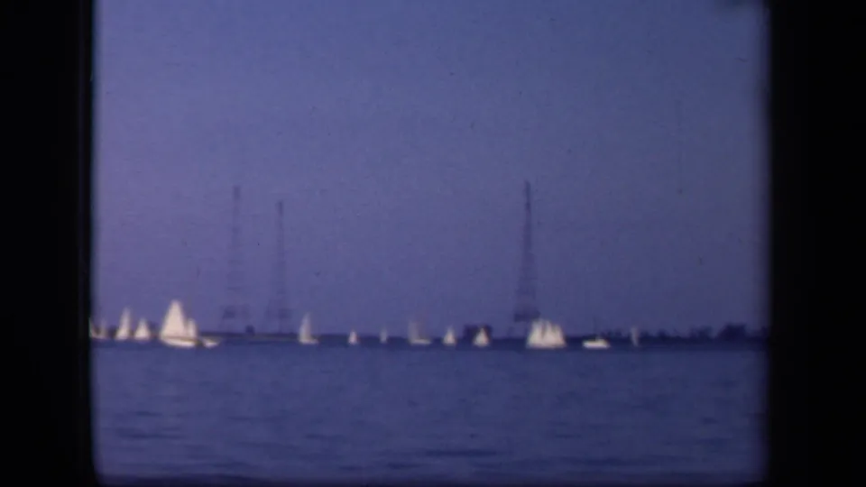 Wide 1943 Washington DC home-movie view of white sailboats across open water, with distant towers and a low shoreline.