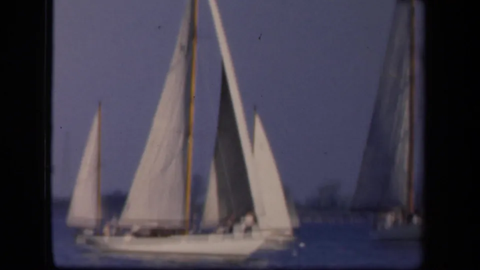 1943 Washington, DC home-movie frame of white sailboats on calm water, with people faintly visible aboard and a soft distant shoreline.