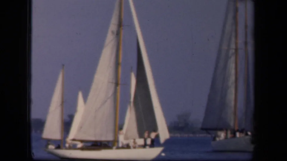 The frame shows sailboats with tall white and darker sails, people standing on deck, and calm water in the 1943 Washington, DC clip.