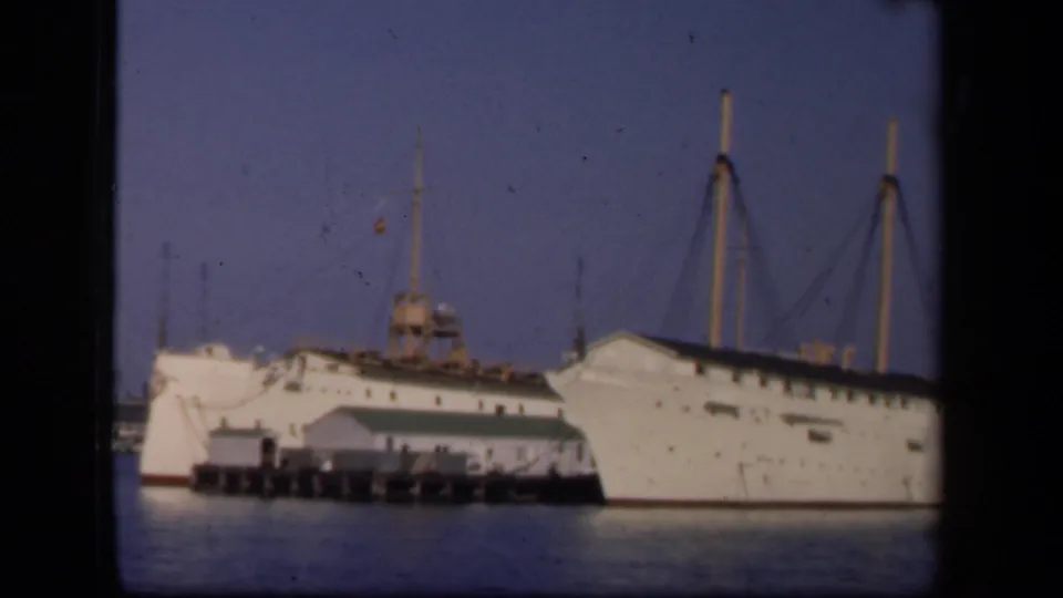 A closer 8mm frame shows the white ship at the pier in Washington, DC, with bow, deck structures, masts, and harbor water visible.