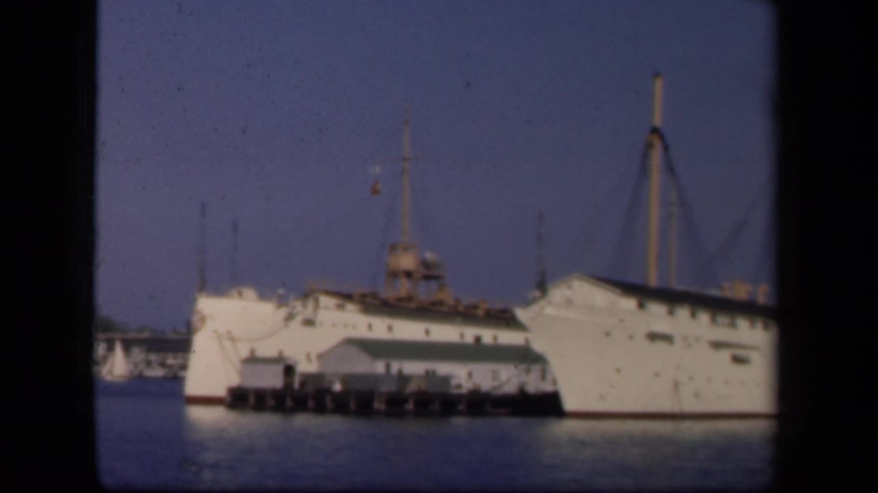 Large white ship docked beside a pier under a blue sky.
