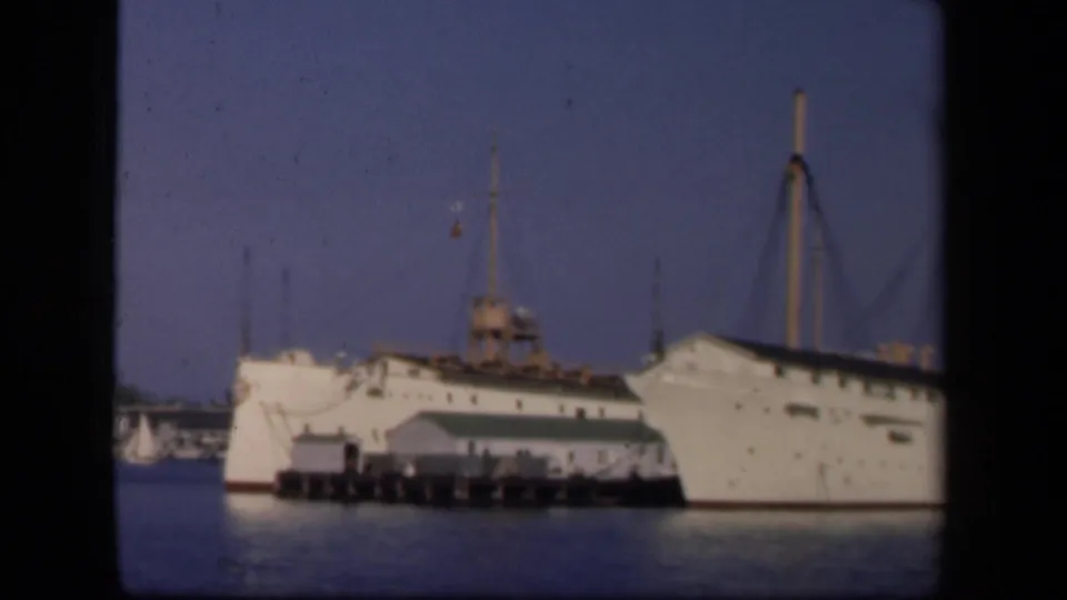 1943 home-movie frame showing a large white ocean liner or passenger ship docked at a pier, with water and black film borders visible.