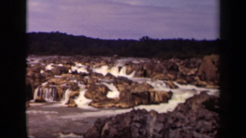 Archival 8mm frame showing multiple small waterfalls and rapids in a rocky Washington, DC river scene.