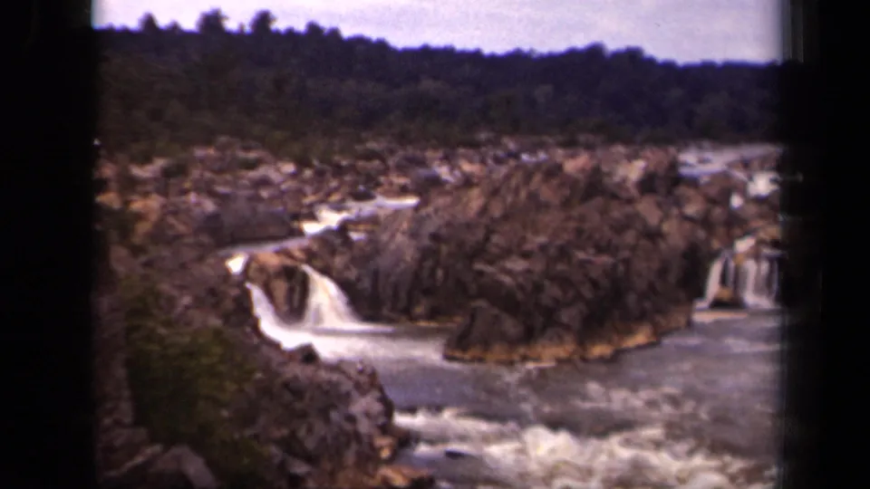 Vintage 8mm frame showing a low waterfall, rough rock formations, and wooded background in the supplied Washington, DC 1943 clip.