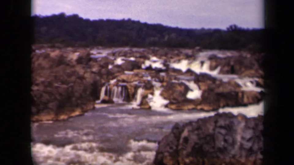 End frame from the 1943 8mm clip showing a rock outcrop, rushing white water, low cascades, and forested hillside in the distance.