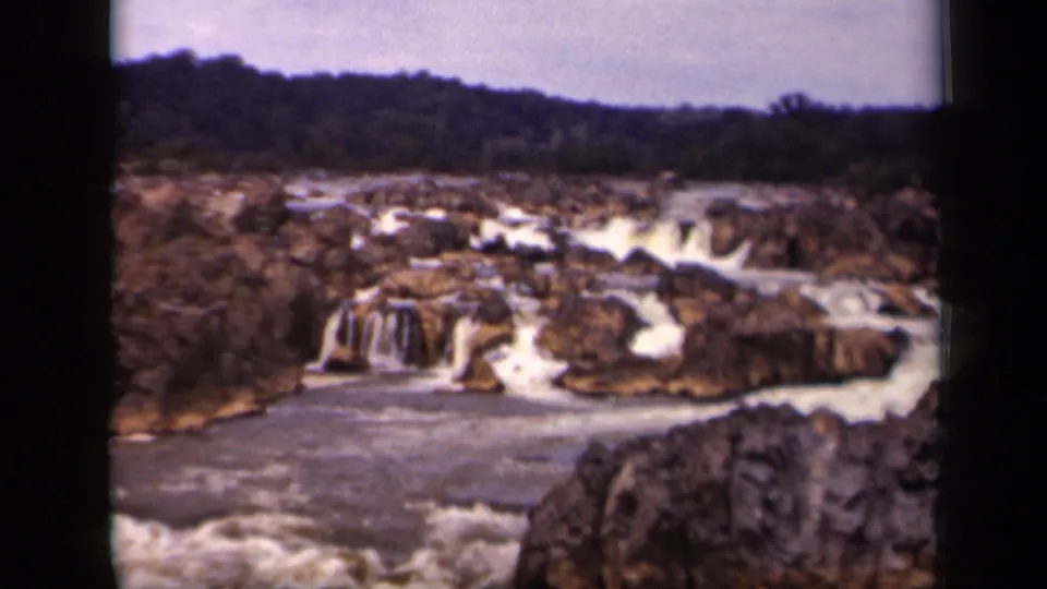 1943 Washington, DC home-movie frame showing whitewater cascading over dark rocks below a wooded ridge.