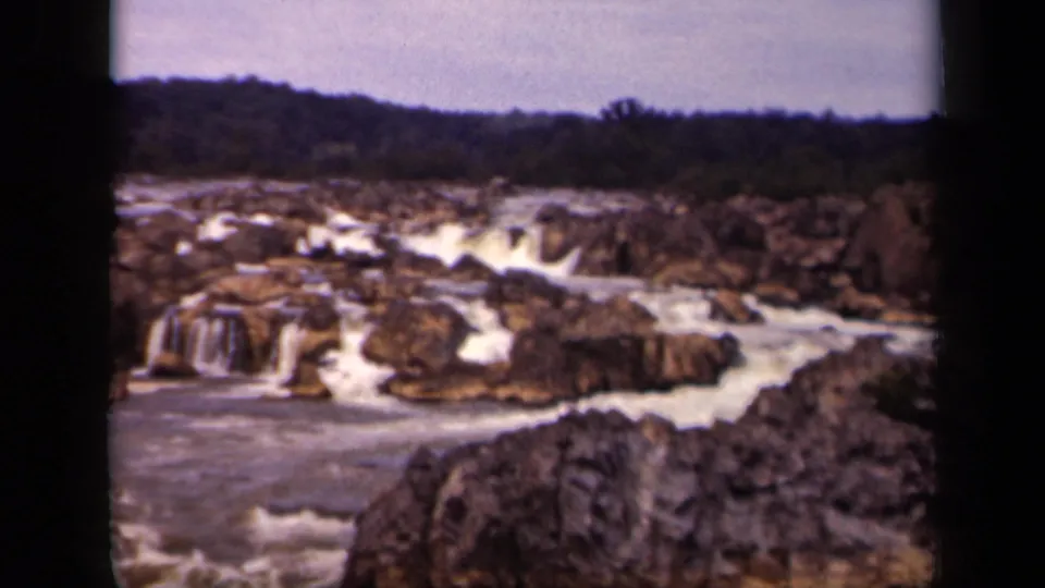 1943 8mm frame with a foreground boulder, rushing water, and layered rocky falls in Washington, DC.
