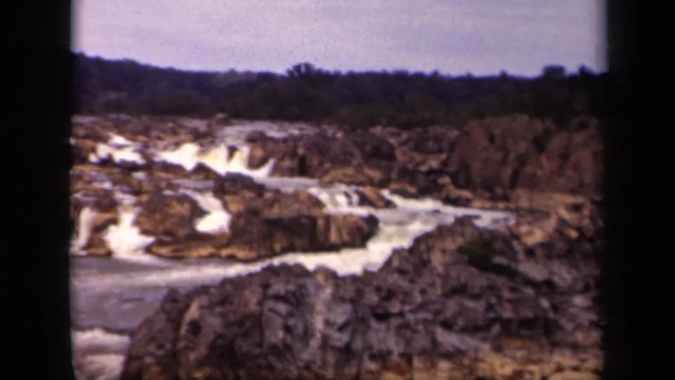 1943 Washington, DC home-movie frame showing a rocky river channel with whitewater, distant trees, and soft 8mm film texture.
