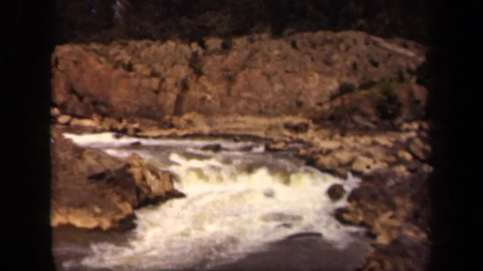 A closer 1943 Washington, DC home-movie view of turbulent water below a rough rock bank, with warm faded color and grain.