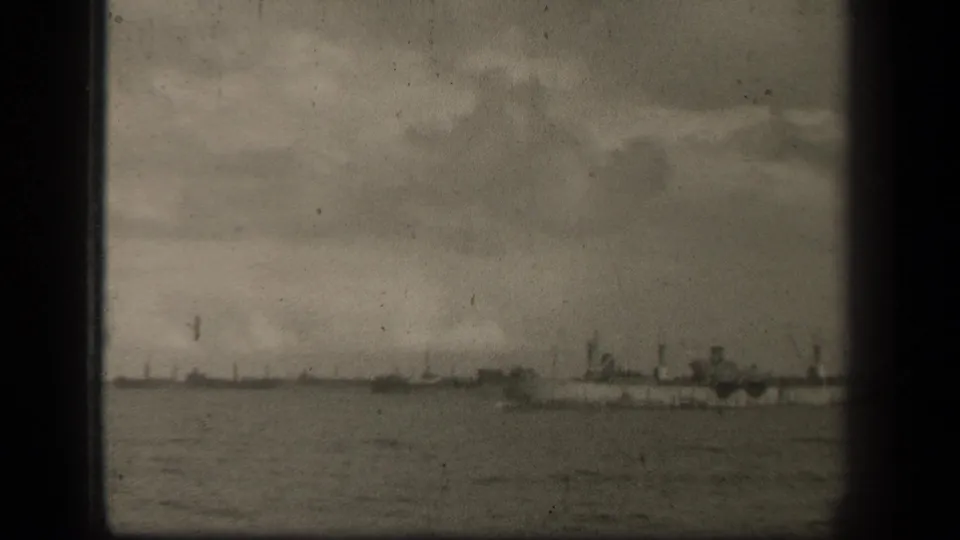 A 1944 Leyte Gulf home-movie frame shows a distant naval line across open water, with dark gate edges and visible film wear.