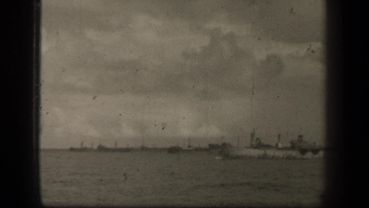 Distant ships on open water beneath a cloudy sky, framed by dark film borders.