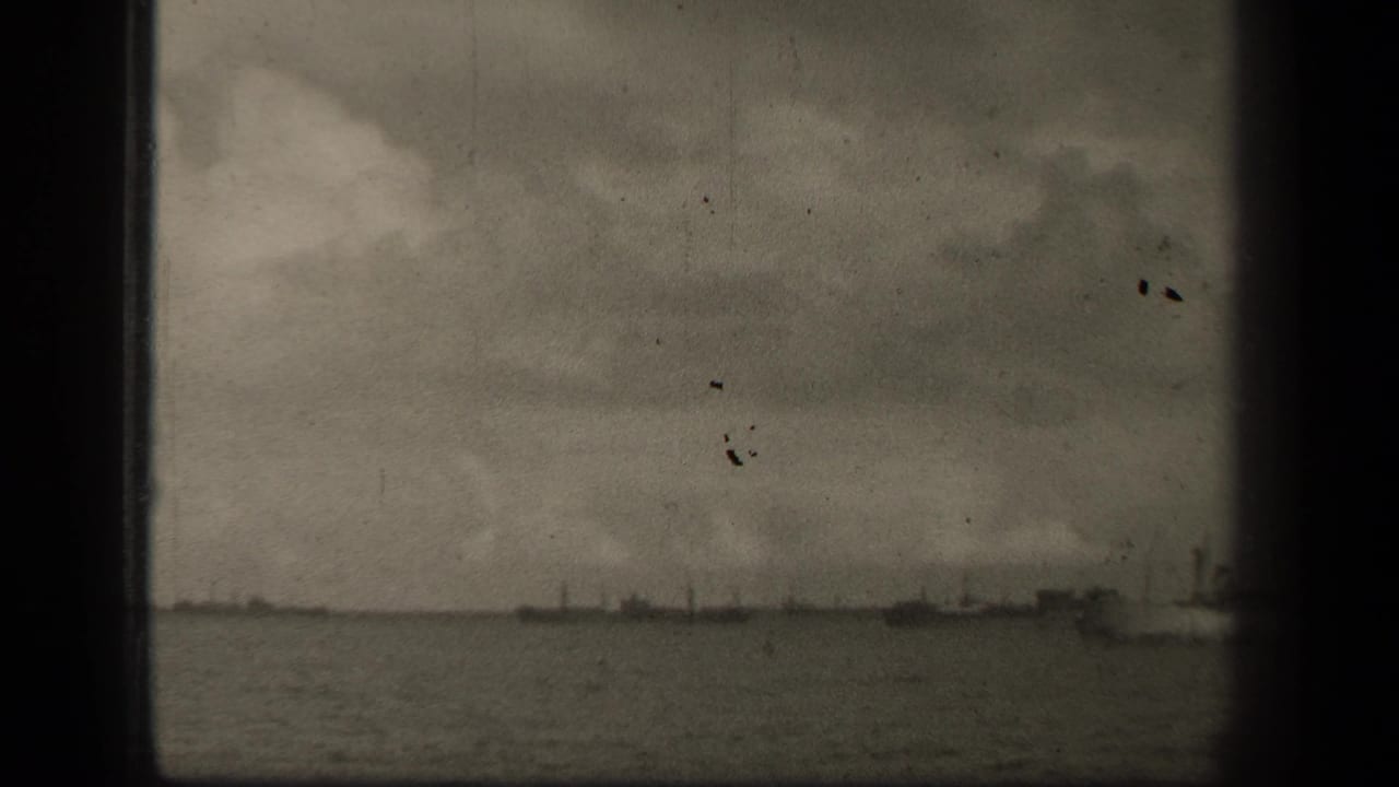 Open water and distant vessel silhouettes under a cloudy sky within a film frame.