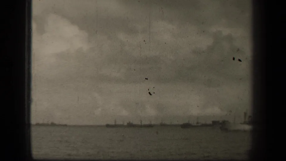The pan continues across Leyte Gulf, with low distant ships and a gray clouded sky visible through aged 8mm film.