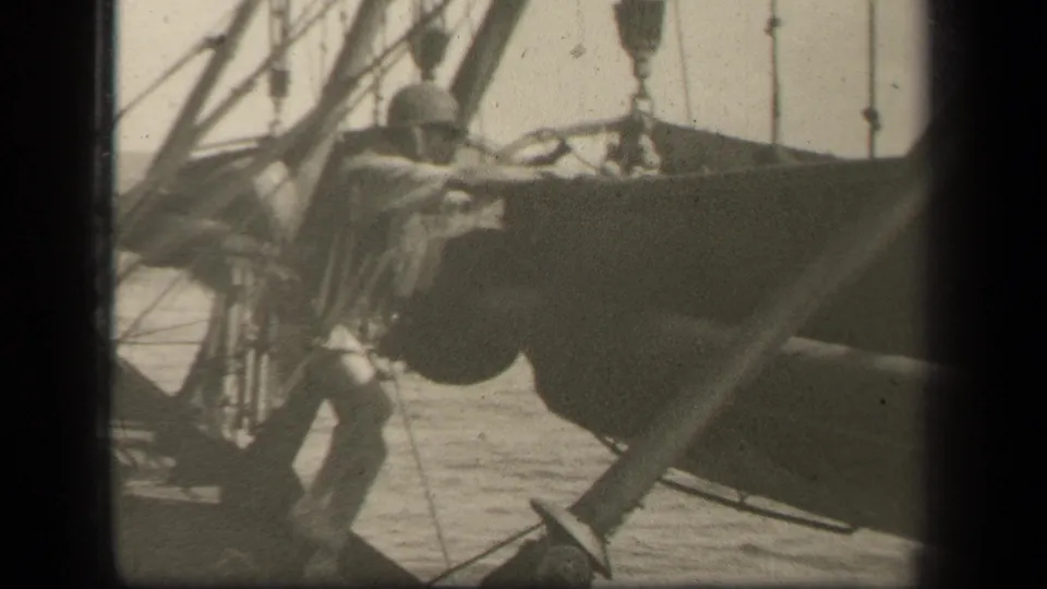A helmeted soldier leans toward the suspended boat on a ship deck in 1944 Leyte Gulf wartime footage.