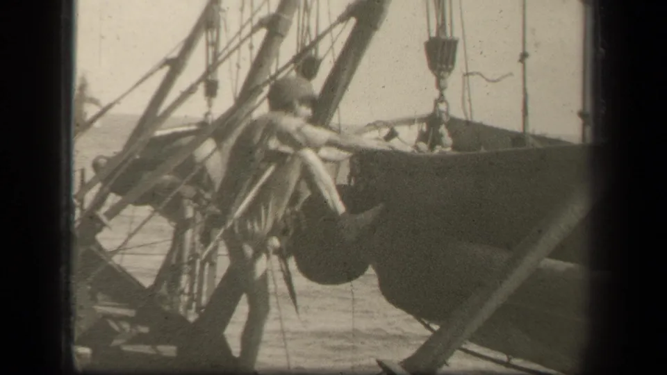 A serviceman in helmet and uniform reaches across naval deck equipment, with rigging, pulleys, and ocean visible in the Leyte Gulf footage.