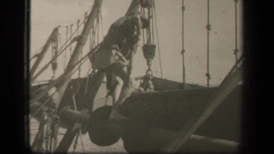 At the end of the clip, the serviceman steps higher over the naval vessel structure, surrounded by rigging, pulleys, and open sea.