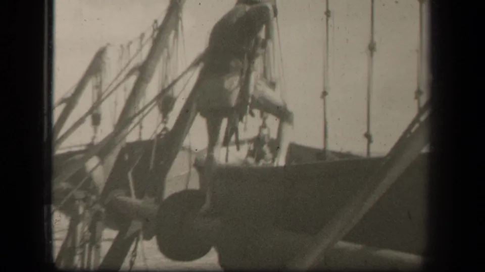 In 1944 Leyte Gulf footage, a man in military-style clothing crouches on a docked sailboat amid ropes and mast lines.
