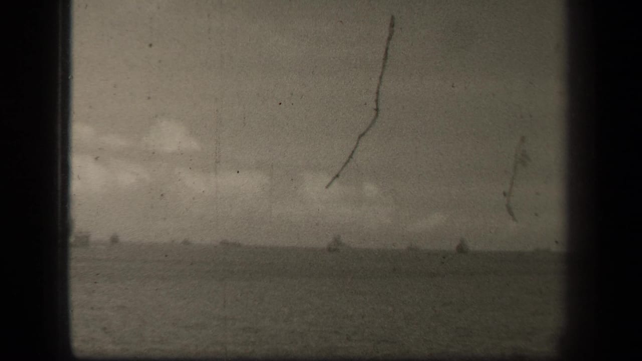 Distant ship silhouettes on a low sea horizon under a cloudy sky, seen through scratched film.