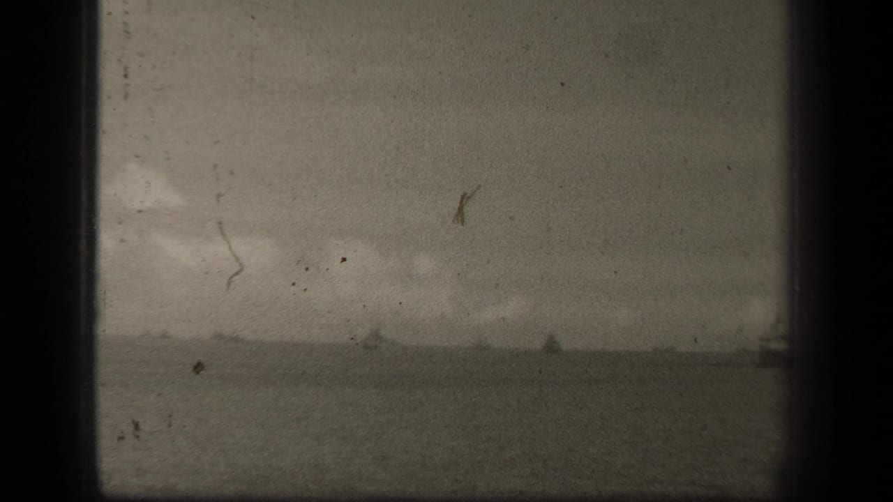 Wide sea horizon with several faint vessel shapes beneath a hazy, clouded sky.