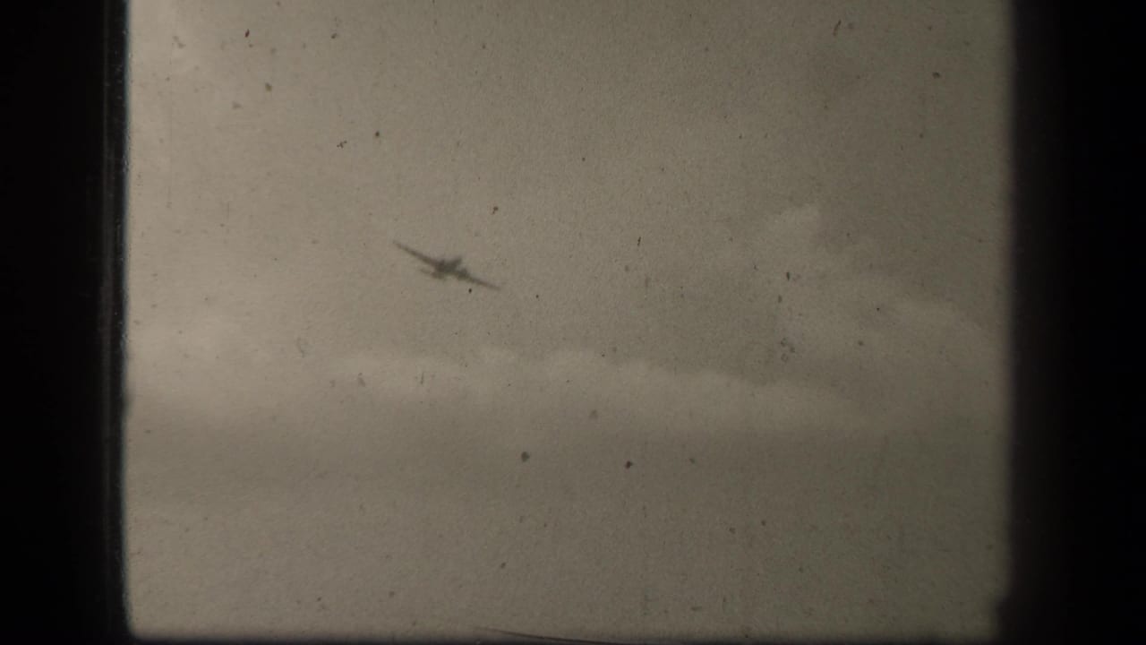 Black-and-white 8mm view of a small aircraft over Leyte Gulf, with cloudy sky and a faint horizon below.