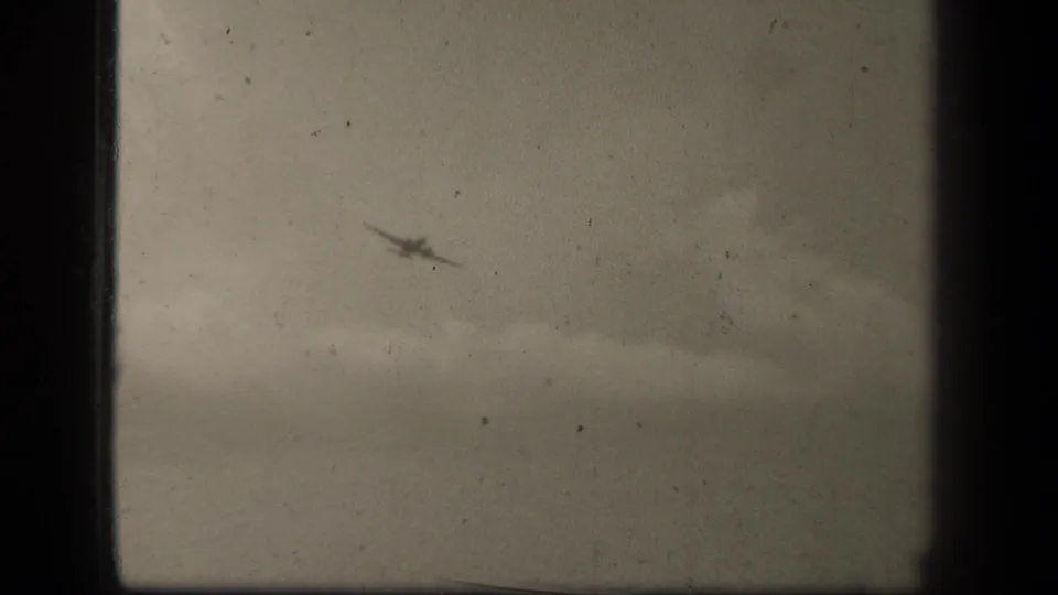 Black-and-white 8mm view of a small aircraft over Leyte Gulf, with cloudy sky and a faint horizon below.