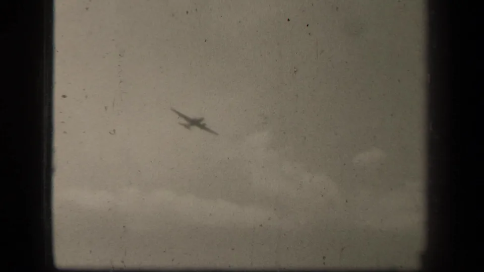 1944 8mm frame from Leyte Gulf showing a blurred aircraft silhouette against clouds above a low water horizon.