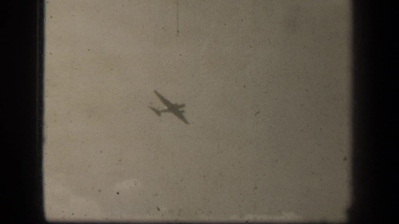 Small airplane silhouette crossing a cloudy sky through aged film grain.