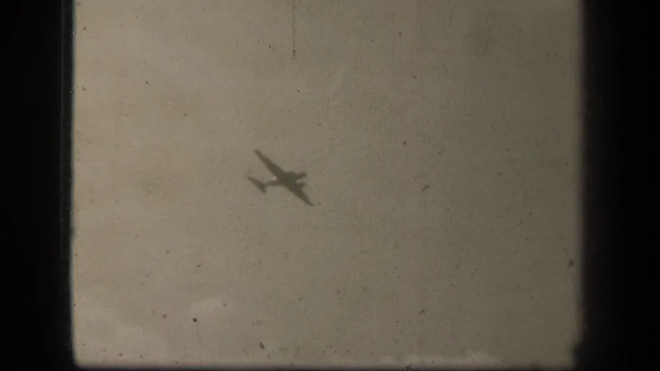 Small aircraft silhouette in cloudy sky, from 1944 Leyte Gulf 8mm footage per supplied metadata.