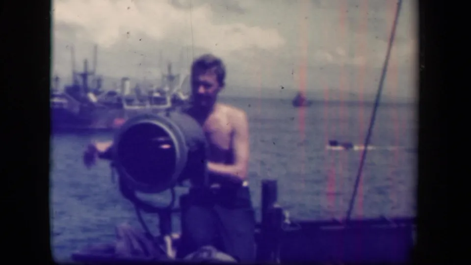 The 8mm frame shows a sailor close to a large searchlight on a vessel, with Leyte Gulf water and distant ships beyond.