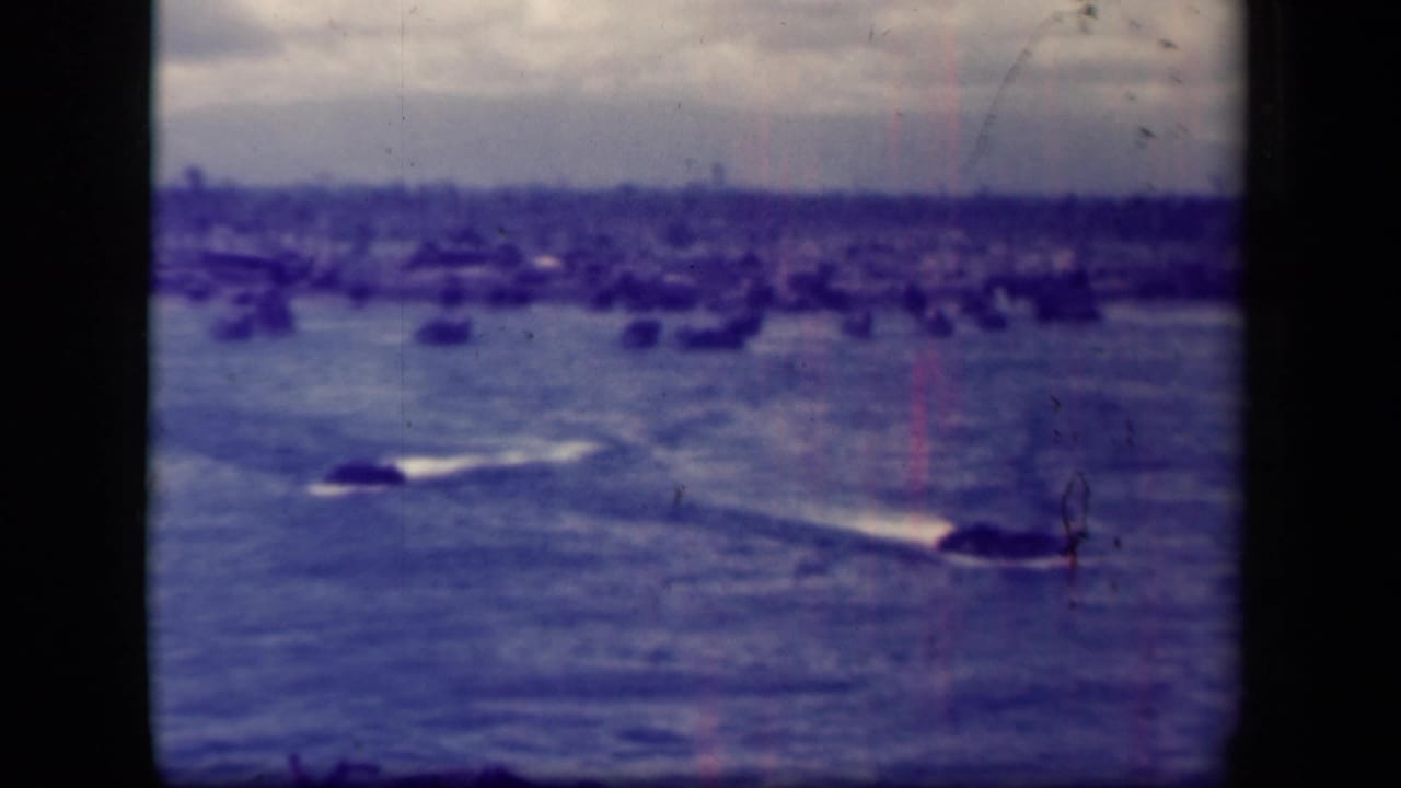 Small dark craft leave wakes across water with many distant vessels along the horizon.