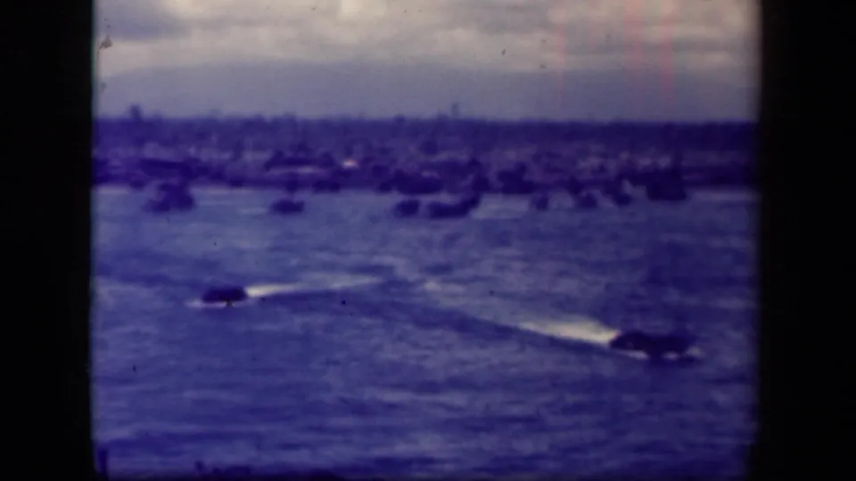 Leyte Gulf water view with two moving craft, long wakes, a hazy shore, and numerous distant ships in soft 8mm color.