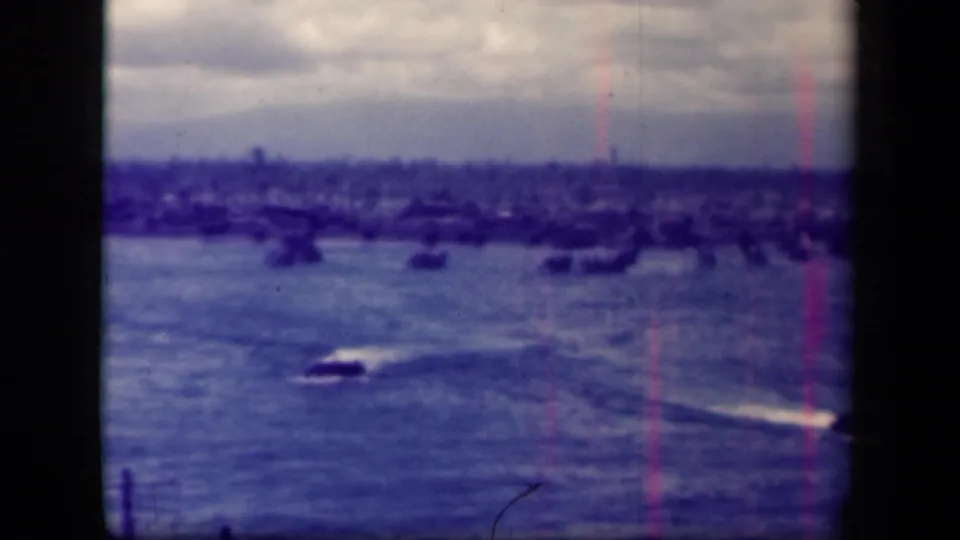 1944 Leyte Gulf 8mm frame showing small craft moving across open water toward a distant shoreline beneath an overcast sky.