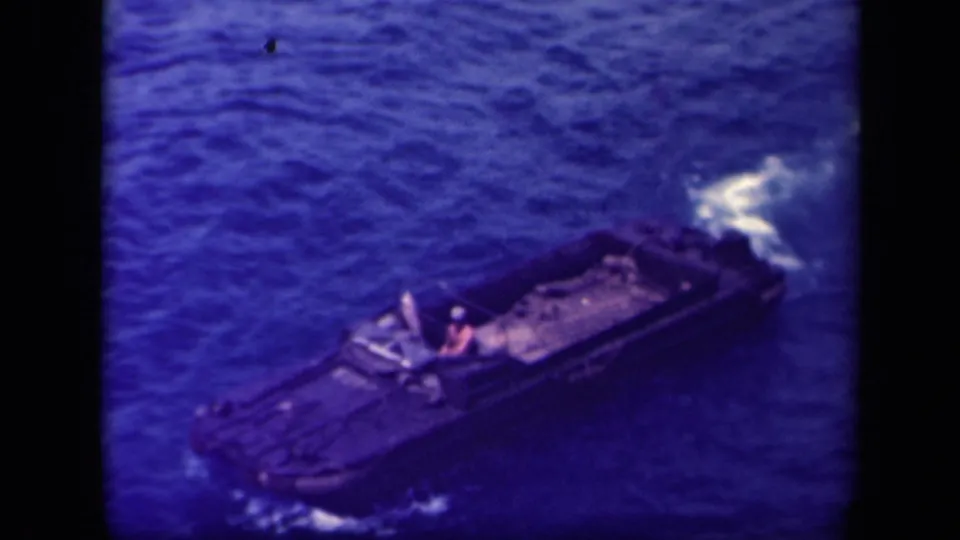 1944 Leyte Gulf 8mm frame of a tracked amphibious craft underway on open water, with wake and a visible person aboard.