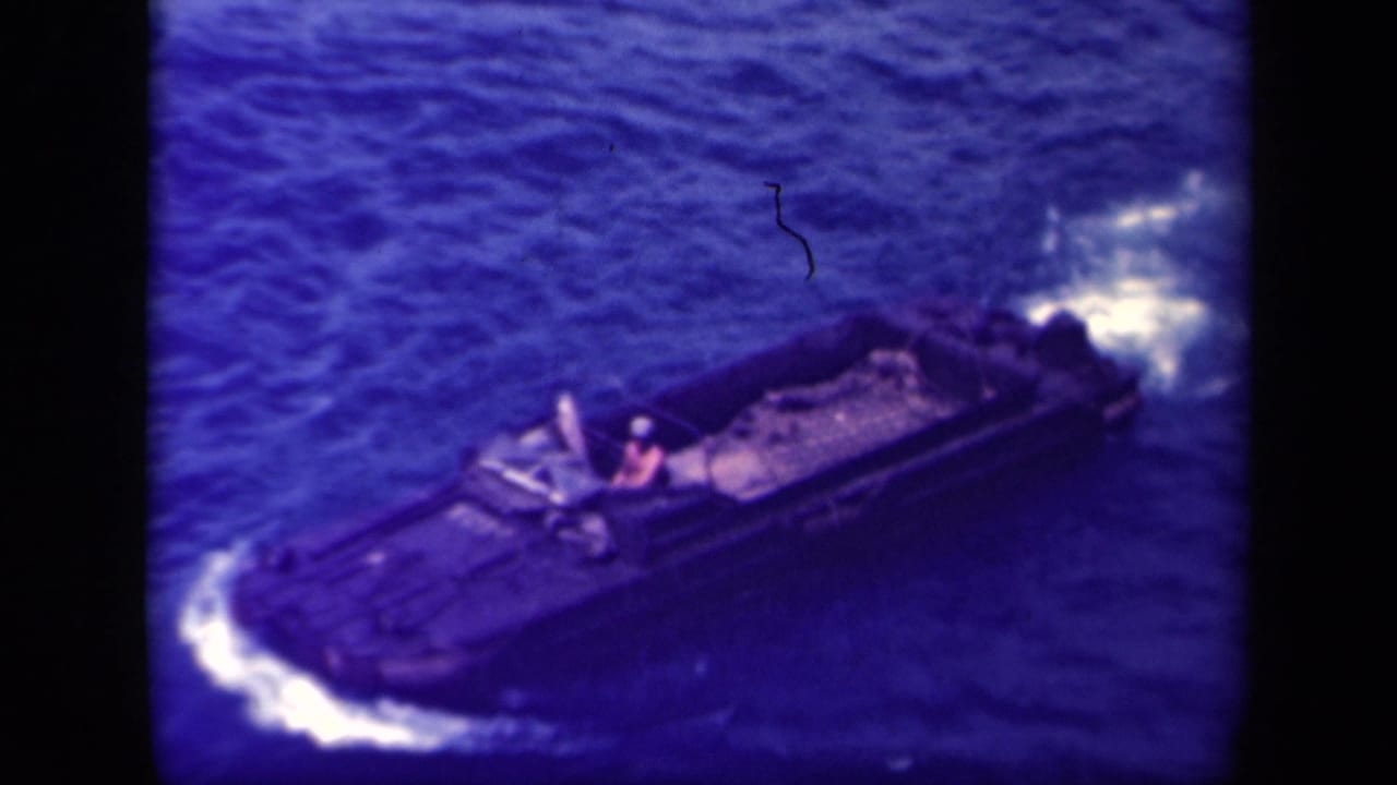 1944 Leyte Gulf 8mm frame showing a dark landing craft underway on choppy blue water with a single figure near the helm.