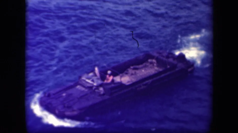1944 Leyte Gulf 8mm frame showing a dark landing craft underway on choppy blue water with a single figure near the helm.