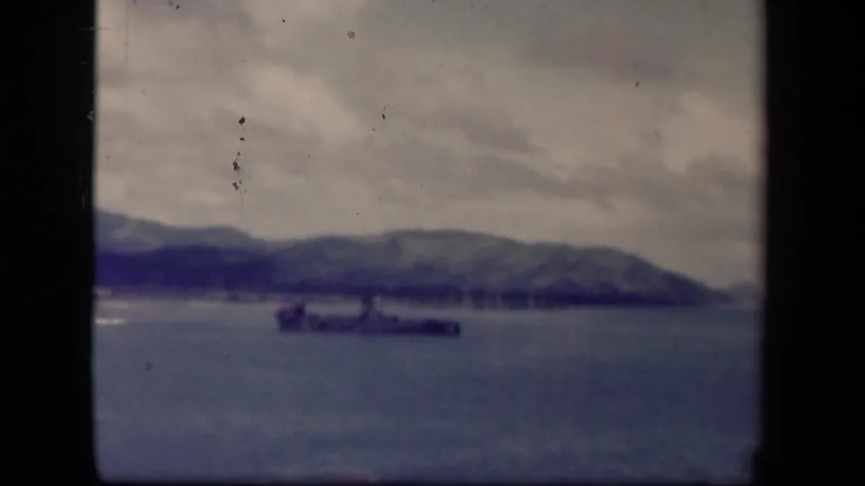 A large warship appears offshore in Leyte Gulf, with blue-gray water, distant hills, cloud cover, and visible 8mm gate edges.