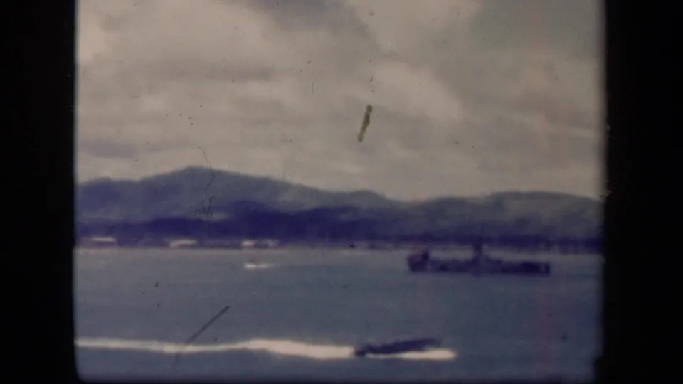 1944 Leyte Gulf 8mm frame showing a low speedboat track, distant offshore vessel, muted water, and cloudy hills.