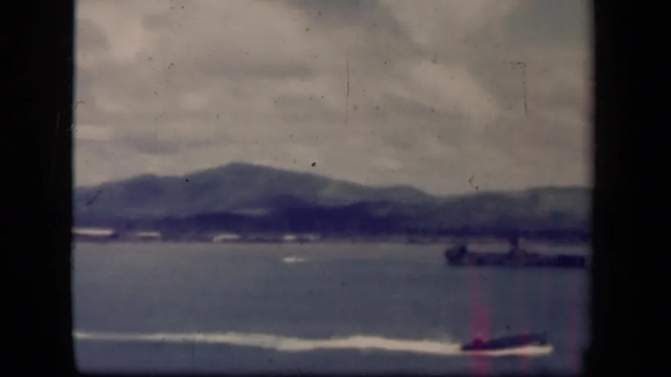 1944 Leyte Gulf 8mm frame with the speedboat near the right edge, a distant vessel, hazy coastal hills, and visible film wear.